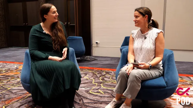 Two women seated facing each other on blue chairs having a conversation