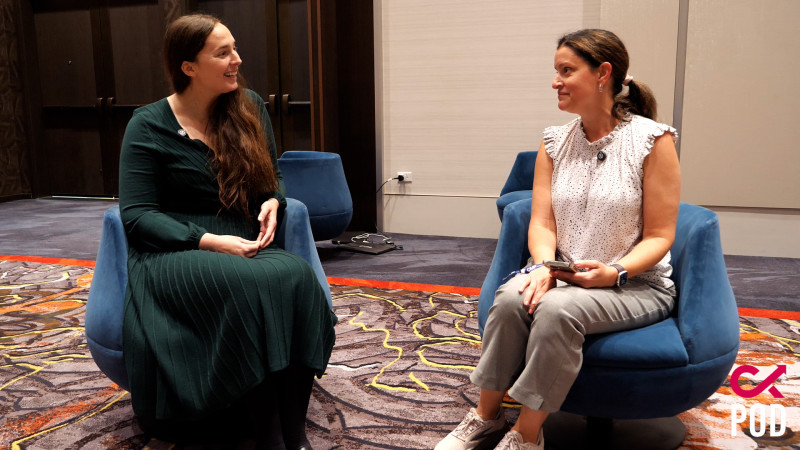 Two women seated facing each other on blue chairs having a conversation